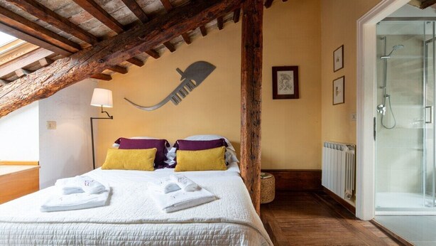 A hotel room with a bed, a wooden ceiling, a wall-mounted lamp, and a glass shower enclosure.