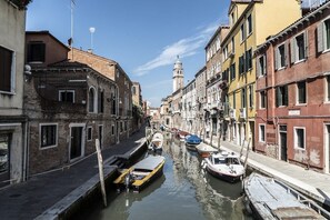 A narrow canal flanked by historic buildings with a tower in the distance. - Altana studio (Venezia)