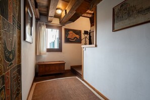A narrow hallway with a wooden bench, a framed artwork on the wall, and a patterned floor. - Altana studio (Venezia)