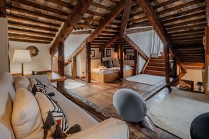 A rustic attic room with exposed wooden beams, a sofa, a chair, and a bed. - Altana studio (Venezia)