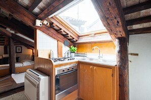 A compact kitchen with a gas stove, oven, and sink, wooden cabinets, and a skylight. - Altana studio (Venezia)