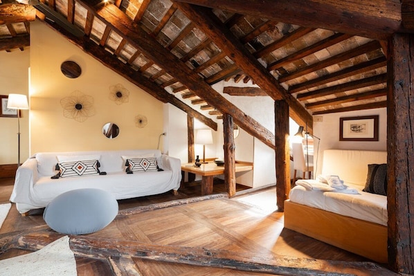 Une pièce rustique avec un plafond en bois, un canapé blanc, un lit et une petite table ronde.