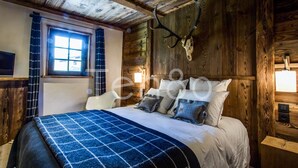 Een slaapkamer met een houten hoofdbord, een bed met een blauw geruit deken, en een raam met gordijnen.