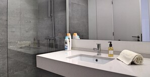 Un bagno moderno con un ampio specchio, un lavandino bianco, un soffione doccia a mano e articoli da toilette sul ripiano.
