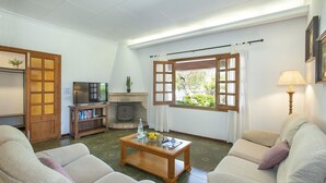 Uma sala de estar com sofá, mesa de centro, televisão, estante de livros e lareira.