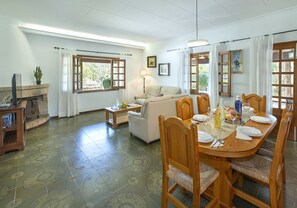 Un comedor con una mesa de madera dispuesta para cuatro personas, un sofá y un televisor en la esquina.