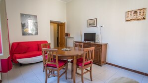 A dining area with a wooden table and chairs, a red sofa, and a television on a cabinet. - Holiday home "Vatican 2 steps" (Roma)