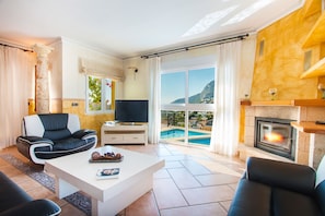 Uma sala de estar com TV, lareira, vista para piscina e varanda.