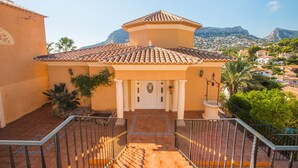 A building with a tiled roof, a central entrance with a door, and a staircase leading to a balcony. - Villa Encanto - PlusHolidays (Calpe)