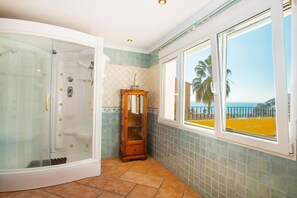 A bathroom with a glass-enclosed shower, a wooden cabinet, and a view of the ocean through a window.