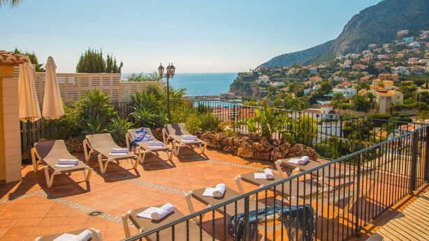 A rooftop terrace with lounge chairs, a pool, and a view of the sea and a hillside town. - Villa Encanto - PlusHolidays (Calpe)