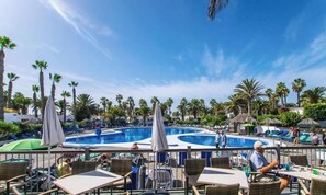 A pool area with lounge chairs and umbrellas, surrounded by palm trees. - Las Brisas 112 | Resort Stay by Villas Now (Playa Blanca)