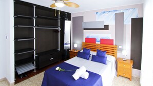Een slaapkamer met een bed, een kledingkast, een plafondventilator, een nachtkastje en een muur met abstracte kunst.