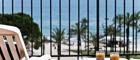 A balcony with a view of the ocean, two glasses of a beverage, and a white chair.