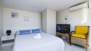 Quarto de hotel com cama, televisão, cadeira e ar condicionado.