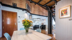 A modern kitchen with a built-in oven, a sink, and a stove. There is a dining area with a wooden table and chairs, and a vase of flowers on the table.
