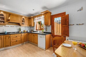 A kitchen with wooden cabinets, a dishwasher, and a dining area with a table and chairs. - Villa Cruz - PlusHolidays (Calpe)