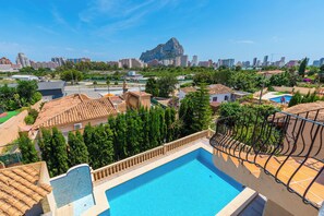 A residential area with a swimming pool, terracotta-tiled roofs, and a view of a cityscape with a prominent mountain in the background. - Villa Cruz - PlusHolidays (Calpe)