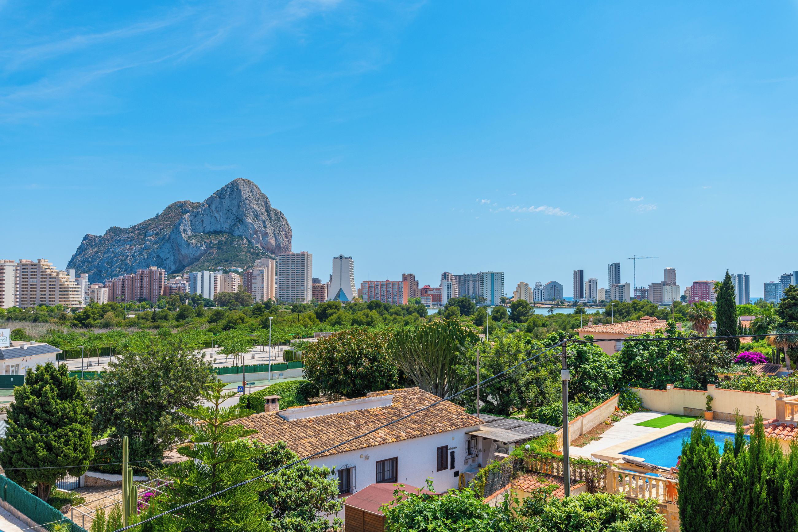 A residential area with a prominent rocky hill, a swimming pool, and a mix of modern and traditional architecture.
