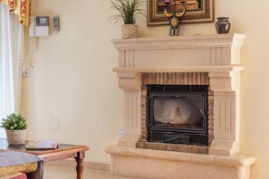 A stone fireplace with a black glass door, a small potted plant on top, and a framed picture above it. - Villa Cruz - PlusHolidays (Calpe)