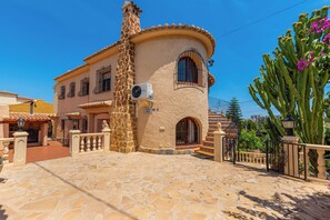 A traditional Mediterranean-style building with a stone facade, a tiled roof, and a courtyard with a stone floor. - Villa Cruz - PlusHolidays (Calpe)