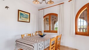 A dining area with a table set for four, surrounded by wooden chairs. - Villa Cruz - PlusHolidays (Calpe)