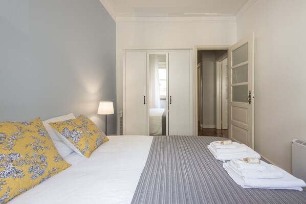 A hotel room with a bed, a bedside lamp, a mirror, and a neatly made bed with towels.