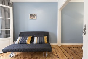 A room with a black sofa, a small framed picture on the wall, and a wooden parquet floor.