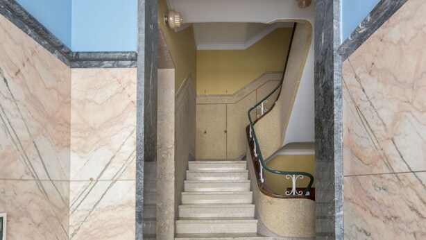 A marble staircase with a handrail, leading to a room with a blue wall and a decorative ceiling.