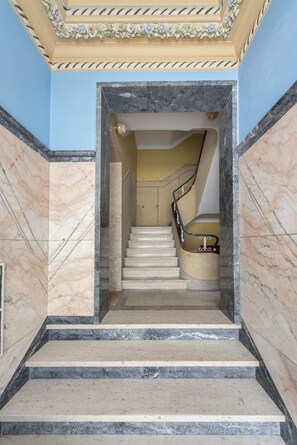 A marble staircase with a handrail, leading to a room with a blue wall and a decorative ceiling.