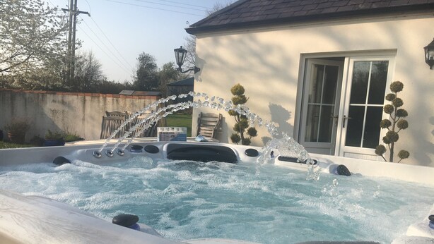 A hot tub with water jets, a wooden deck, and a house in the background.