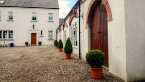 A courtyard with a gravel path, a white building with a red door, and potted plants.