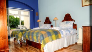 A bedroom with a bed, two bedside lamps, and a window with a view of parked cars and greenery outside.
