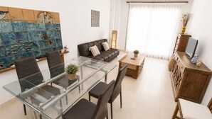 Een moderne woonkamer met een glazen eettafel, een donker leren bank en een groot abstract schilderij aan de muur.