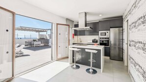 Eine moderne Küche mit einer zentralen Kochinsel, Edelstahlgeräten und Blick auf eine Terrasse.