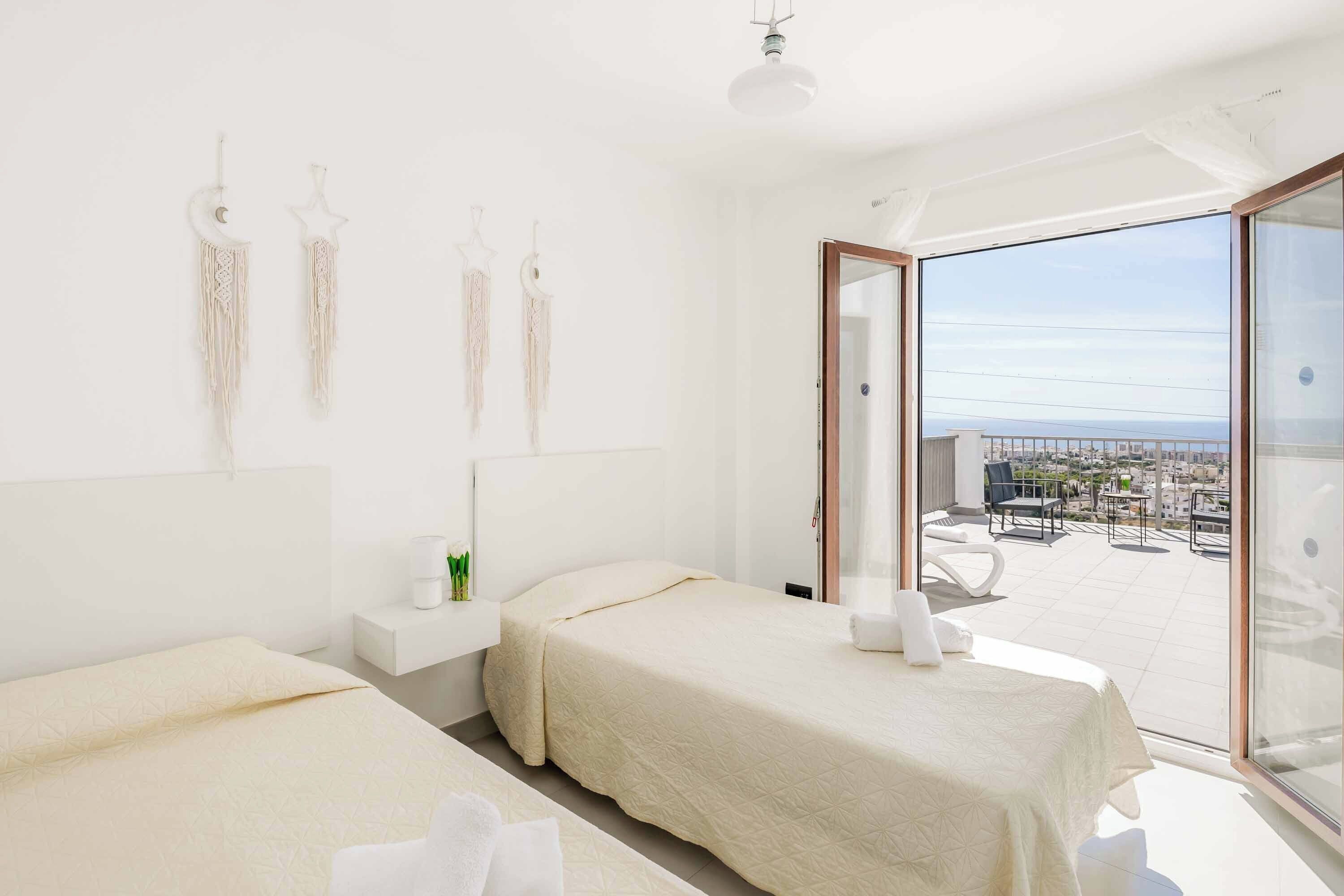A modern hotel room with two beds, a balcony with a city view, and a large window.