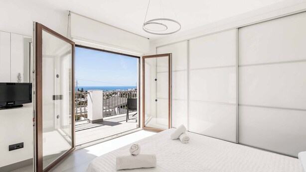 Ein modernes Schlafzimmer mit einem großen Bett, einem Fernseher und einem Balkon mit Meerblick.