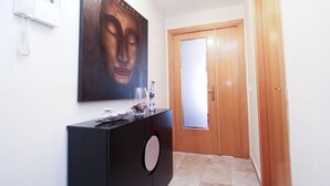 Un pasillo con una puerta de madera, un mueble negro con un jarrón y un vaso, y un cuadro en la pared.