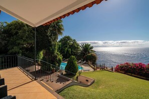 A terrace with a pool, outdoor seating, and a view of the sea.
