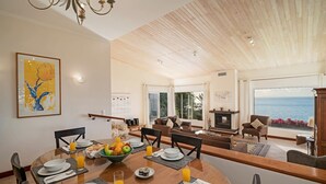 A dining area with a wooden table set for breakfast, a fireplace, and a view of the sea.