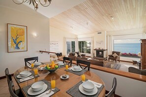 A dining area with a table set for breakfast, a view of the sea, and a living room with a fireplace.