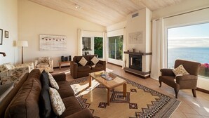 A spacious living room with a fireplace, large windows offering a view of the sea, and a cozy seating area.