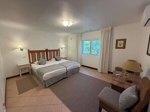 A bedroom with two beds, a nightstand, a chair, a window with curtains, and a ceiling light.
