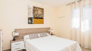 A bedroom with a wooden headboard, a bed with a patterned bedspread, a nightstand with a lamp, and a wall-mounted artwork.