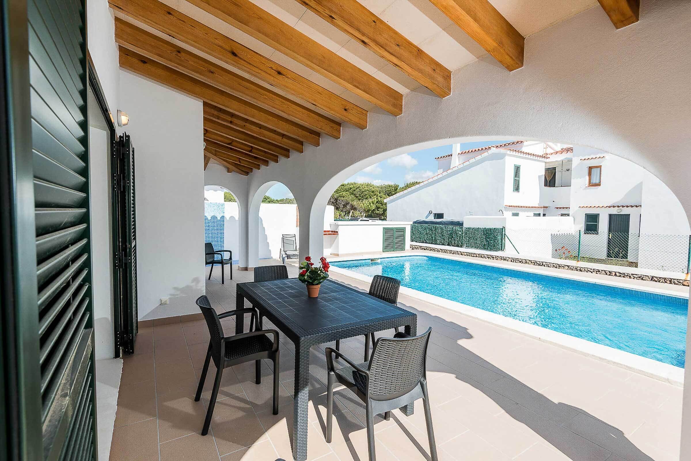 An outdoor patio with a pool, wooden ceiling beams, and a view of white buildings.