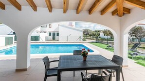 A covered patio with a pool, outdoor seating, and a view of a white building.