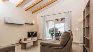 A modern living room with a sofa, a coffee table, and a TV. There is a sliding glass door leading to an outdoor area.