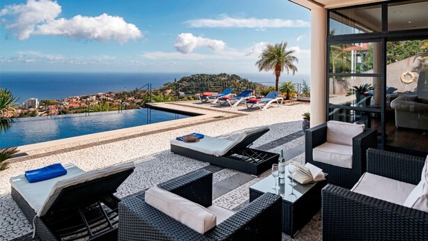 A poolside area with lounge chairs, a table, and a view of the sea and hills. - Fabulous seaview, pool and games room | Villa Luz (Funchal)