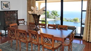 A dining room with a large wooden table and chairs, a vase with flowers, and a view of the ocean through large windows. - Fabulous seaview, pool and games room | Villa Luz (Funchal)
