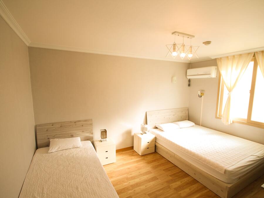 A bedroom with two single beds, a nightstand, a bedside table, a hanging light fixture, and a window with curtains.